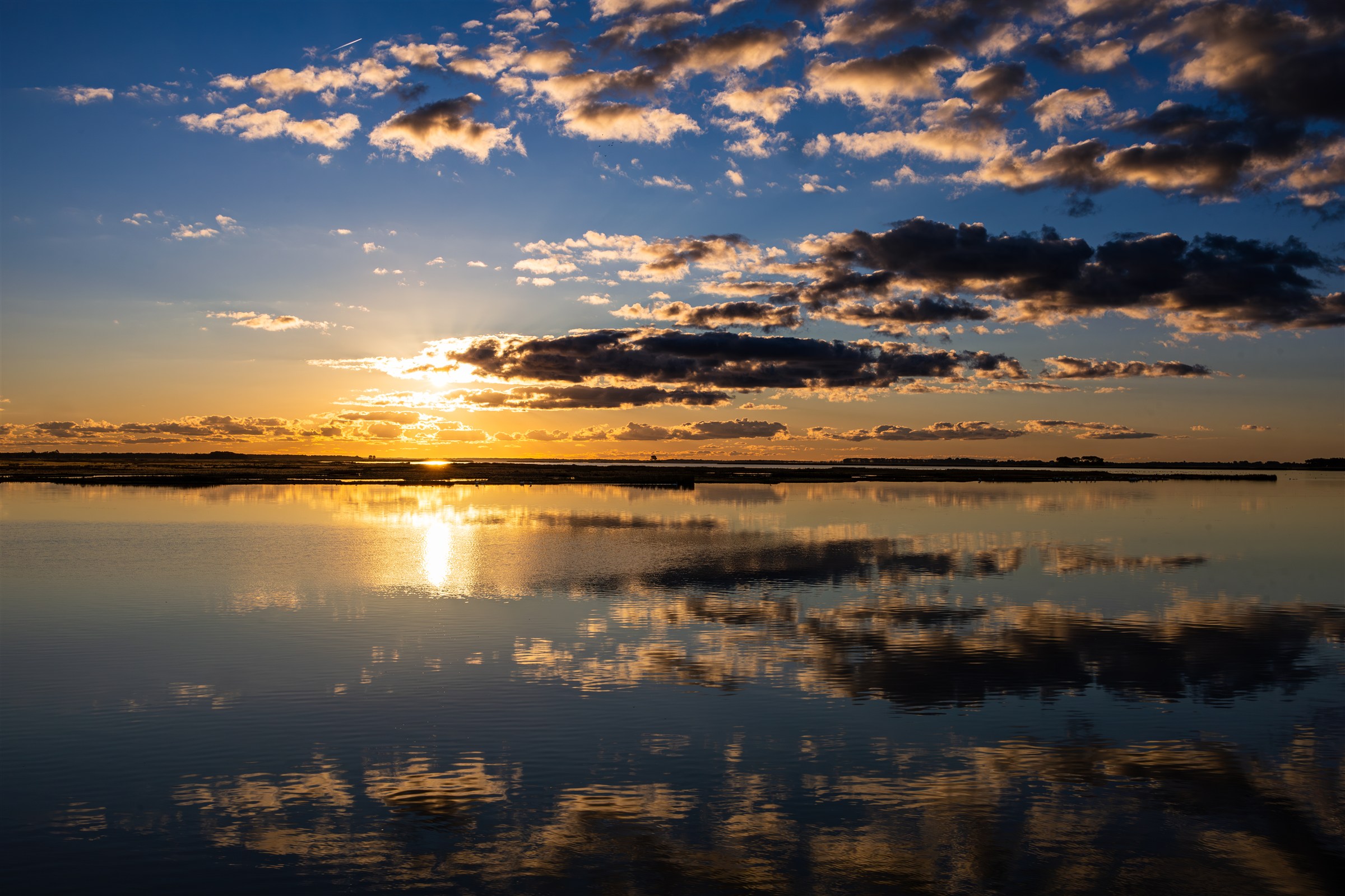 Sonnenuntergang über ruhigem Wasser mit Wolken und ihrer Spiegelung